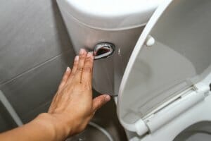 A large caucasian hand is pushing a lever down to flush a toilet.