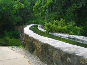 Acequia Espada aqueduct surrounded by local San Antonio vegetation. The acequia is full of water.