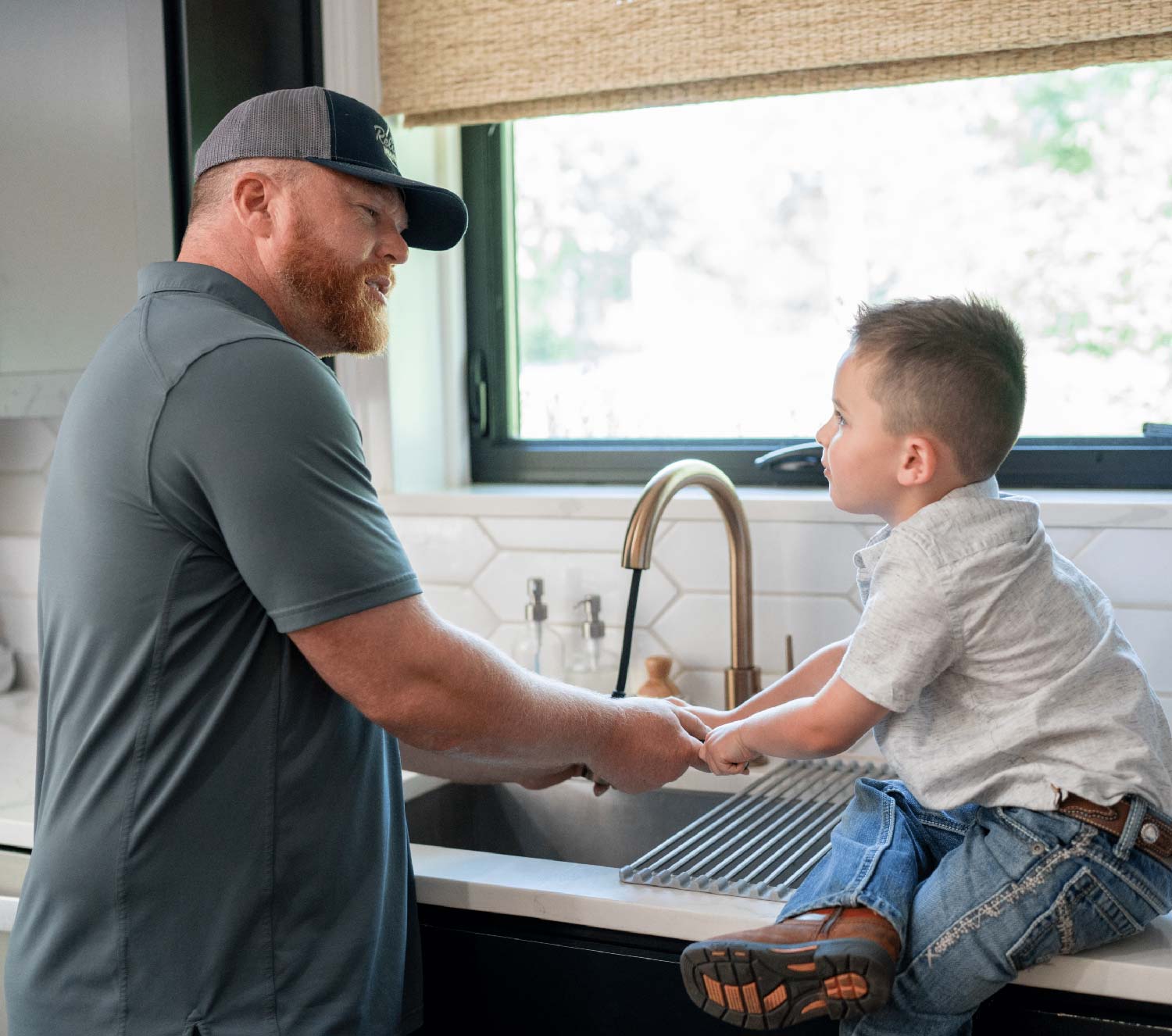 plumber in a residential home interacting with young son sitting at the sink learning about plumbing fictures